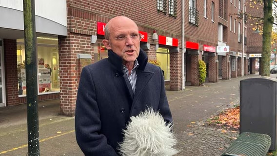 Klägeranwalt Hennemann gibt ein Interview vor einer Sparkassenfiliale